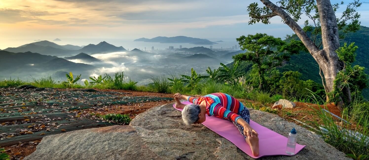 a old lady doing yoga on a hilltop near a tree and a beautiful landscape