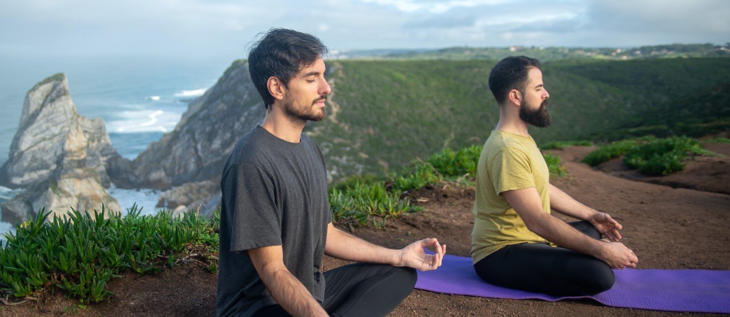 Two men doing yoga on hilltop near a sea in bali
